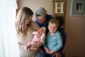 A family gathers together near a window to admire their newborn baby.