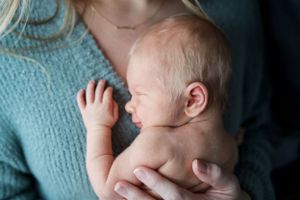 A tender moment showing a newborn baby being cradled in soft blue knit clothing.