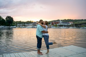 A romantic proposal moment unfolds on a wooden dock by the water during sunset.