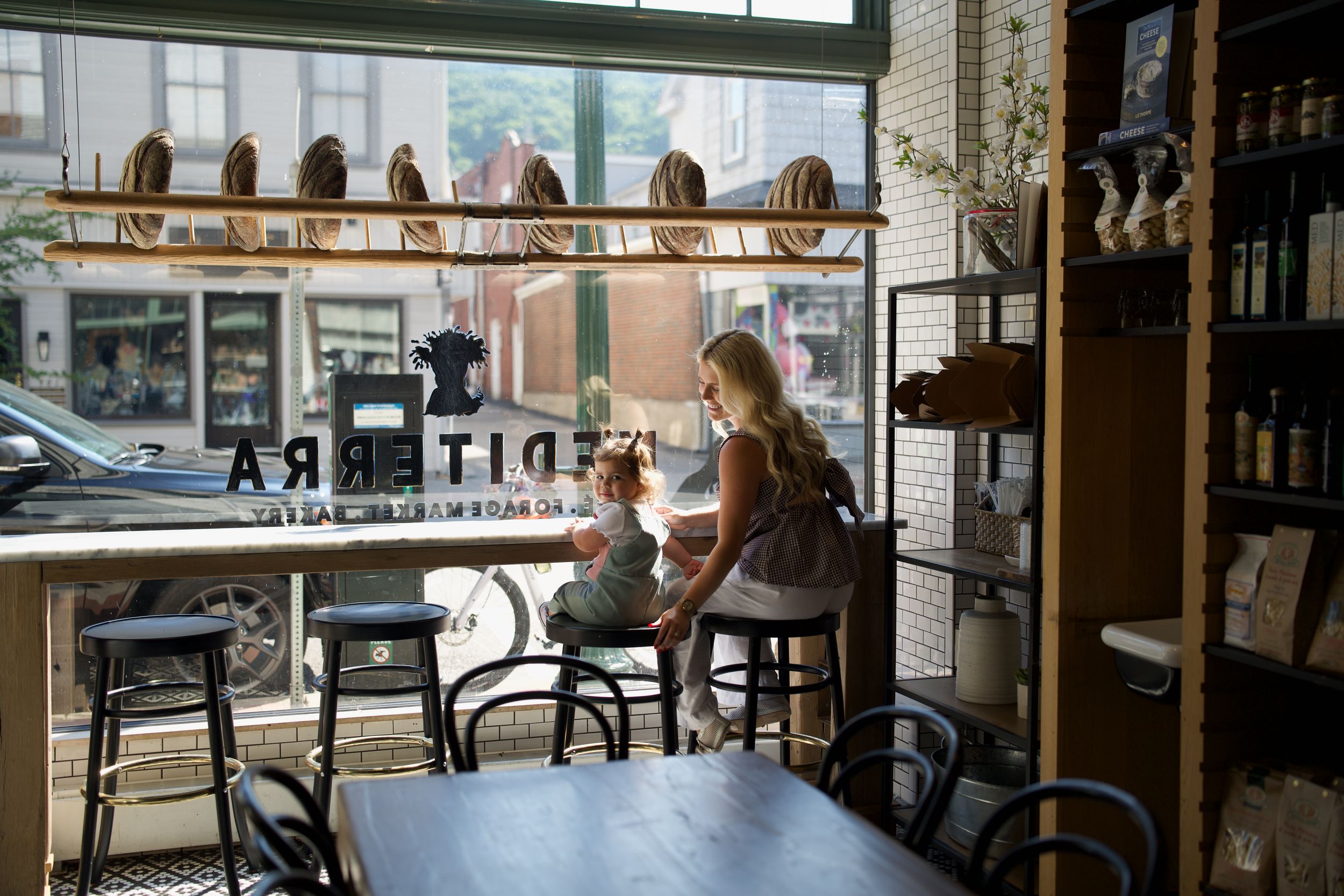 A row of people sit at a window counter inside a diner or restaurant with a view of the street outside.
