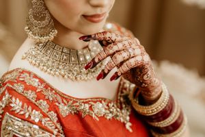 Traditional Indian bridal jewelry and henna-adorned hands with a red and gold embroidered wedding outfit.