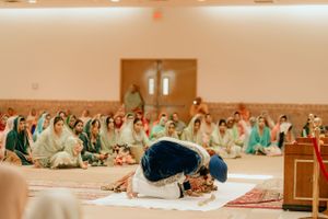 Traditional Sikh wedding prayer ceremony with guests seated on floor in religious setting.