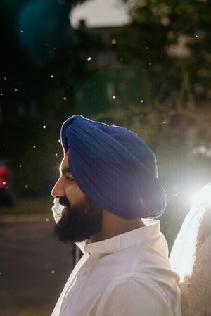 Sikh groom in blue turban and white attire photographed at night with bokeh lights.