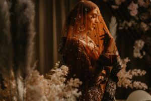 Traditional Indian bride wearing a red veil and ornate jewelry in moody lighting.