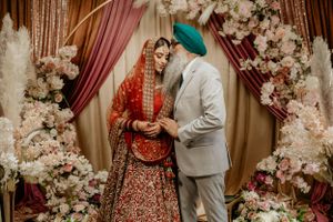 Sikh wedding couple in traditional attire under floral arch during ceremony.