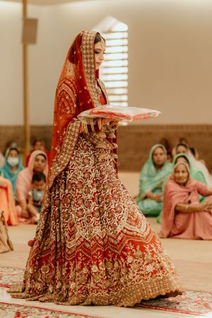A bride in an ornate red lehenga during a traditional Sikh wedding ceremony.