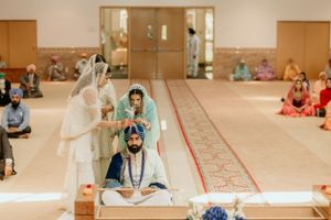 A traditional Sikh wedding ceremony taking place in a Gurdwara with guests seated on the floor.