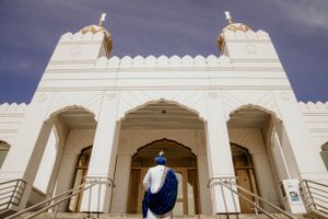 Exterior view of a white Gurdwara with golden domes against a cloudy sky.
