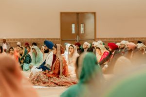 Traditional Sikh wedding ceremony with guests seated on floor in colorful attire during religious service.