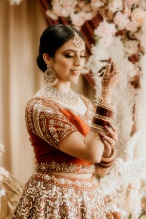Traditional Indian bridal portrait showcasing intricate jewelry and henna designs against floral backdrop.