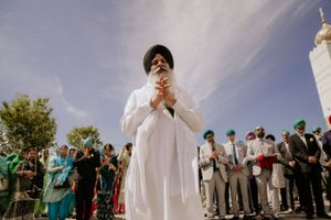 A person in traditional white attire participates in a Sikh prayer ceremony outdoors.