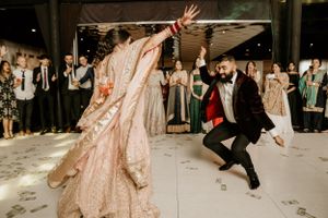 A couple performing an energetic dance move in traditional wedding attire.