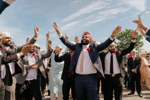 Wedding celebration with joyful guests raising hands outdoors under blue sky.