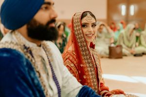 Traditional Sikh wedding couple seated during ceremonial proceedings with ornate attire.