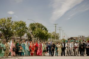 Large wedding party in colorful traditional attire gathered outside under blue sky.