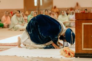 Traditional Sikh prayer ritual being performed on a carpeted floor during a ceremony.