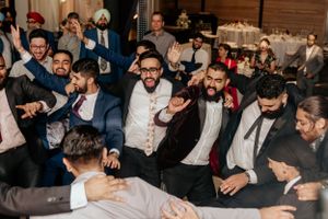 Male guests dancing and celebrating in a circle during a lively wedding reception.
