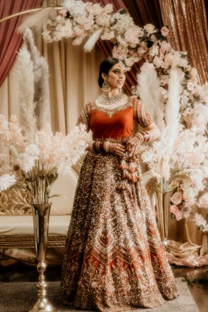 Traditional Indian bridal look with red and gold lehenga surrounded by white floral decorations.