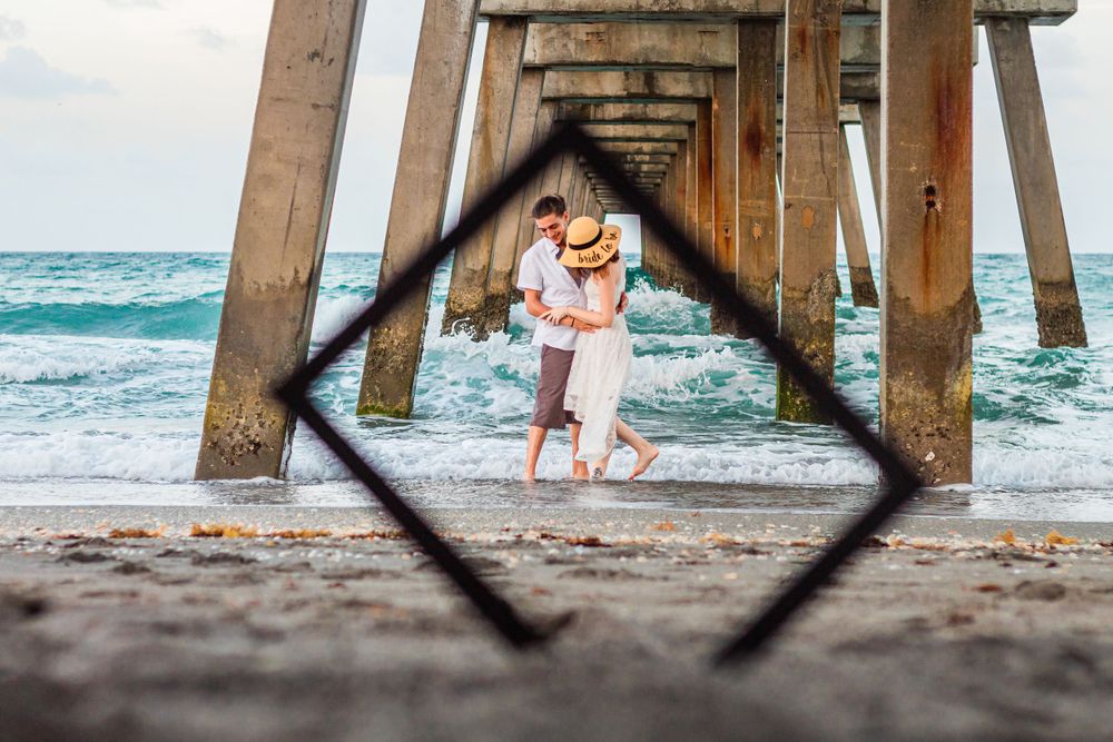 Creative framed beach photo of couple through pier supports with ocean waves at Juno beach pier.