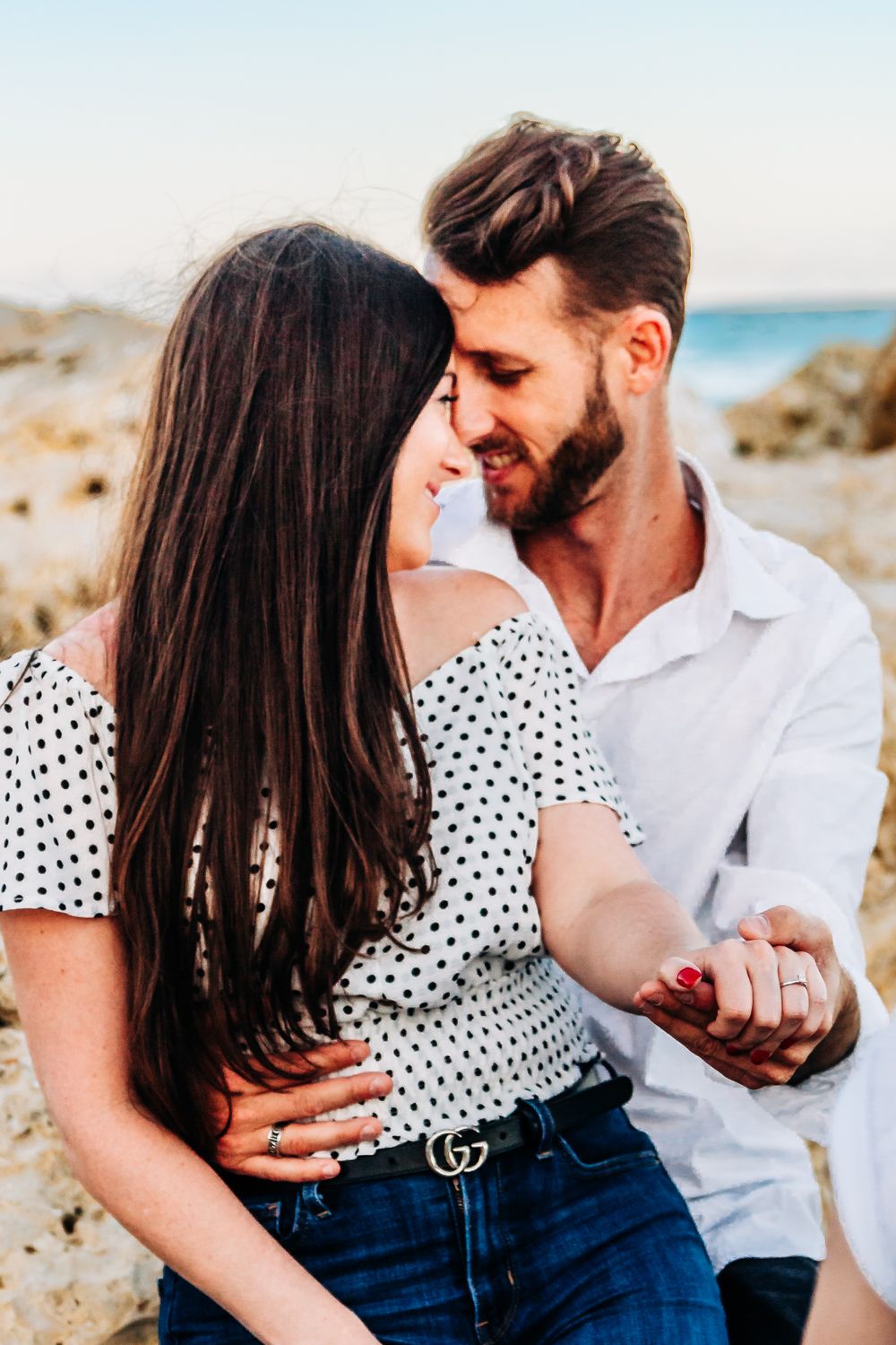 Couple sharing intimate moment on rocky coastal landscape in matching polka dot and white outfits at in palm beach, beach, worth ave