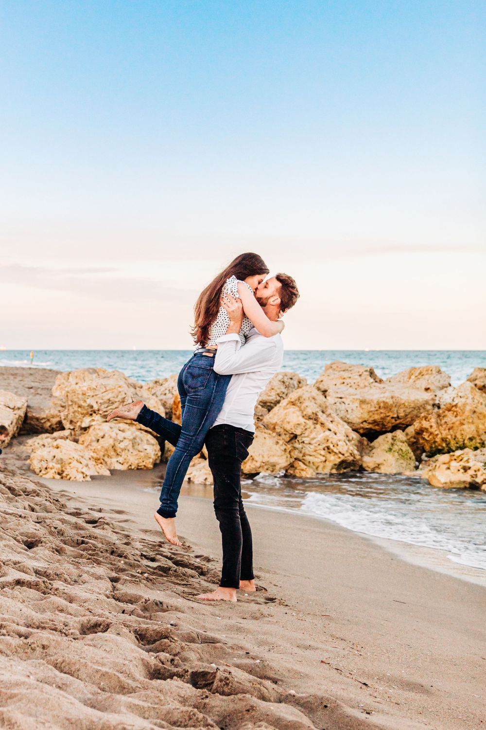 Couple embracing on beach with man lifting woman against sunset ocean backdrop in palm beach Florida on the beach.