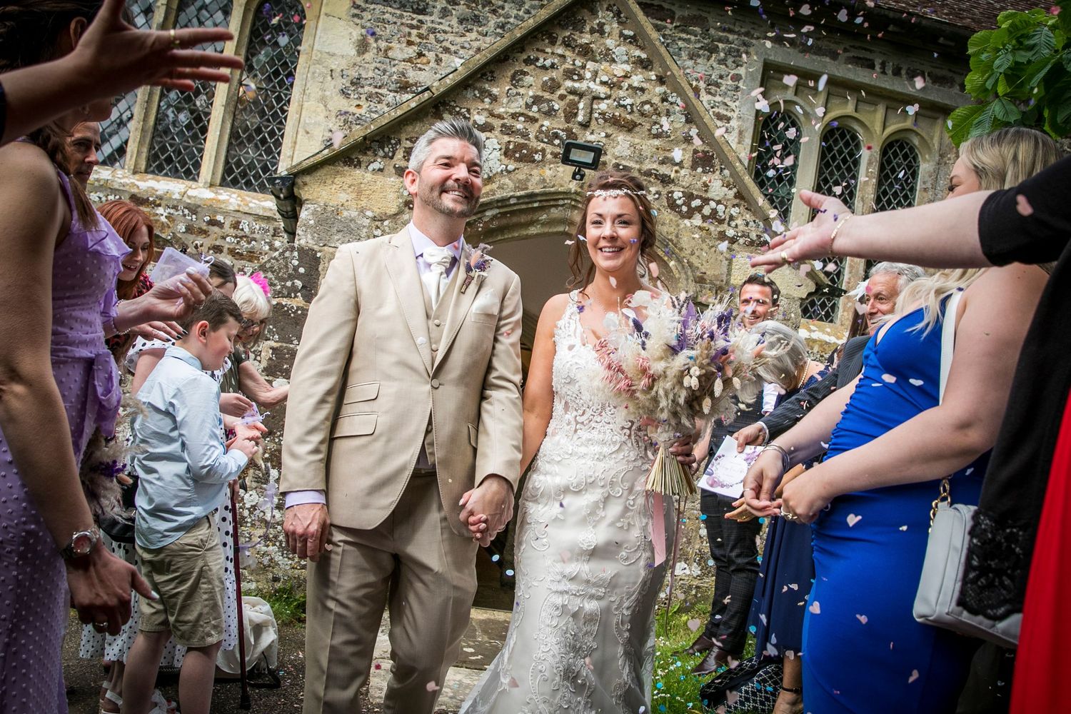 Wedding party celebrates with confetti outside historic stone church.