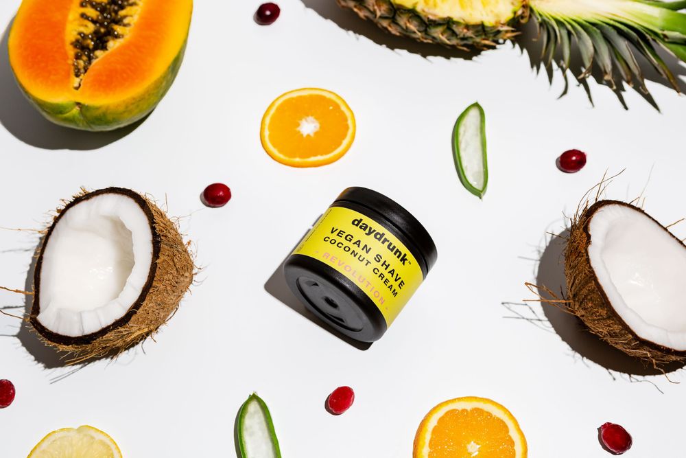 Jar of cream surrounded by coconut, pineapple, citrus, aloe vera and cranberries
