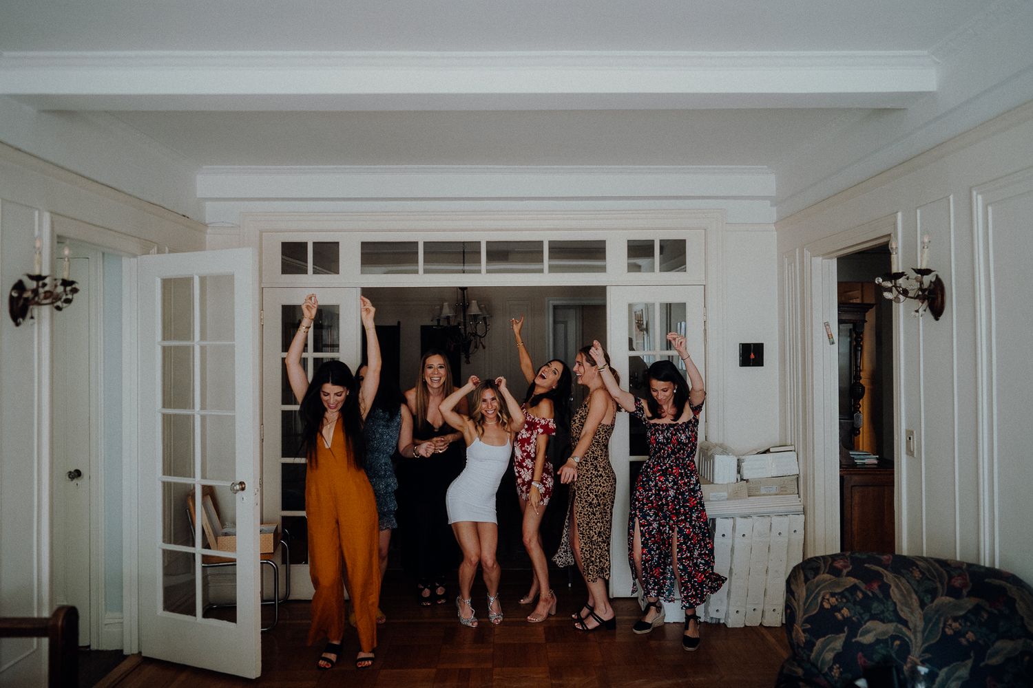 A group of people dancing and celebrating together in a bright white room with French doors.