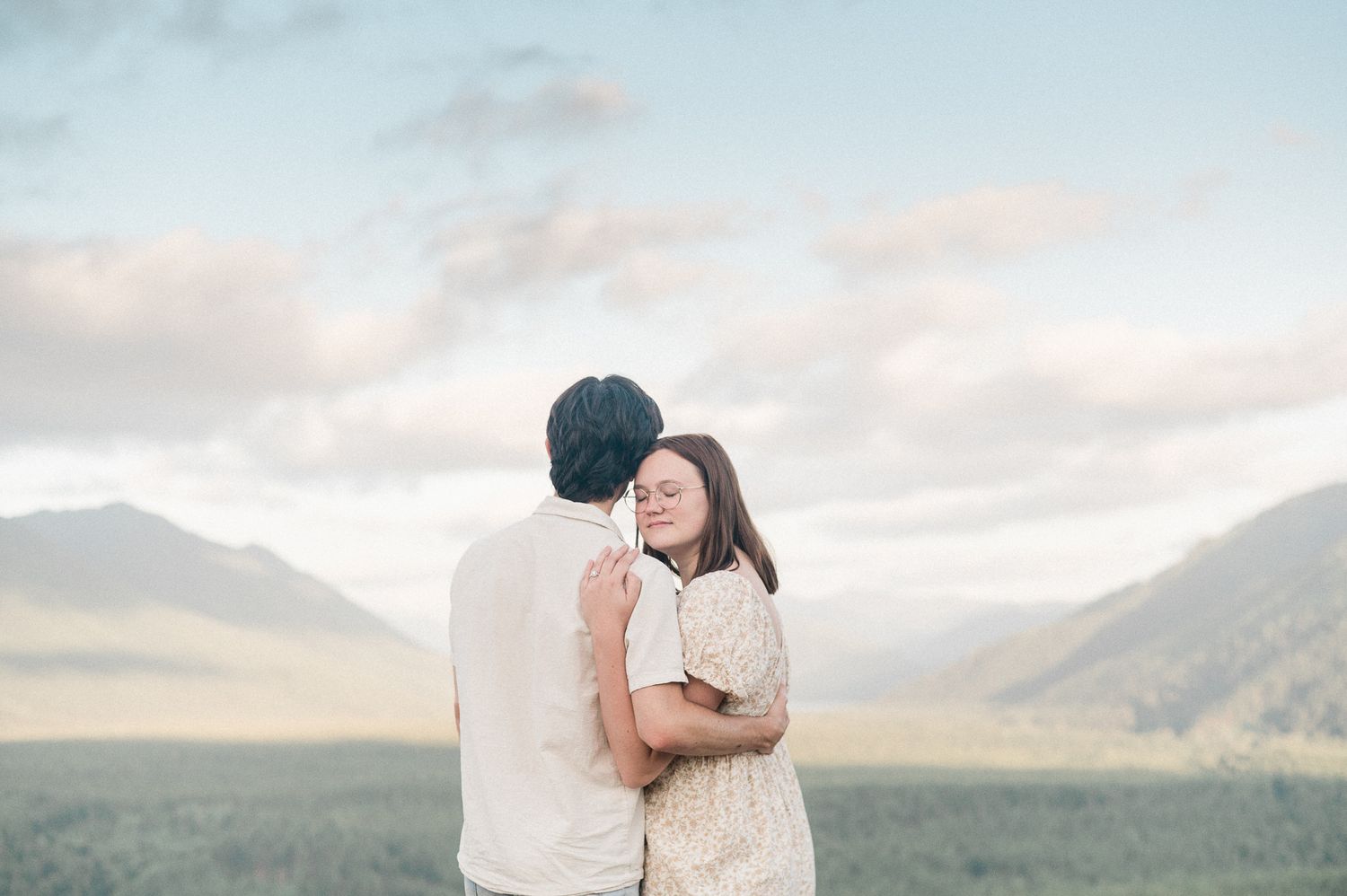 A couple embraces on a scenic mountain path during sunset with dramatic cloudy skies in the background.