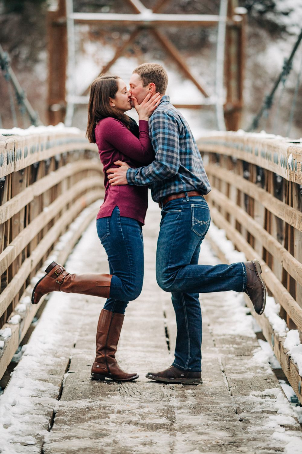 A romantic couple sharing a kiss on a snowy wooden bridge.