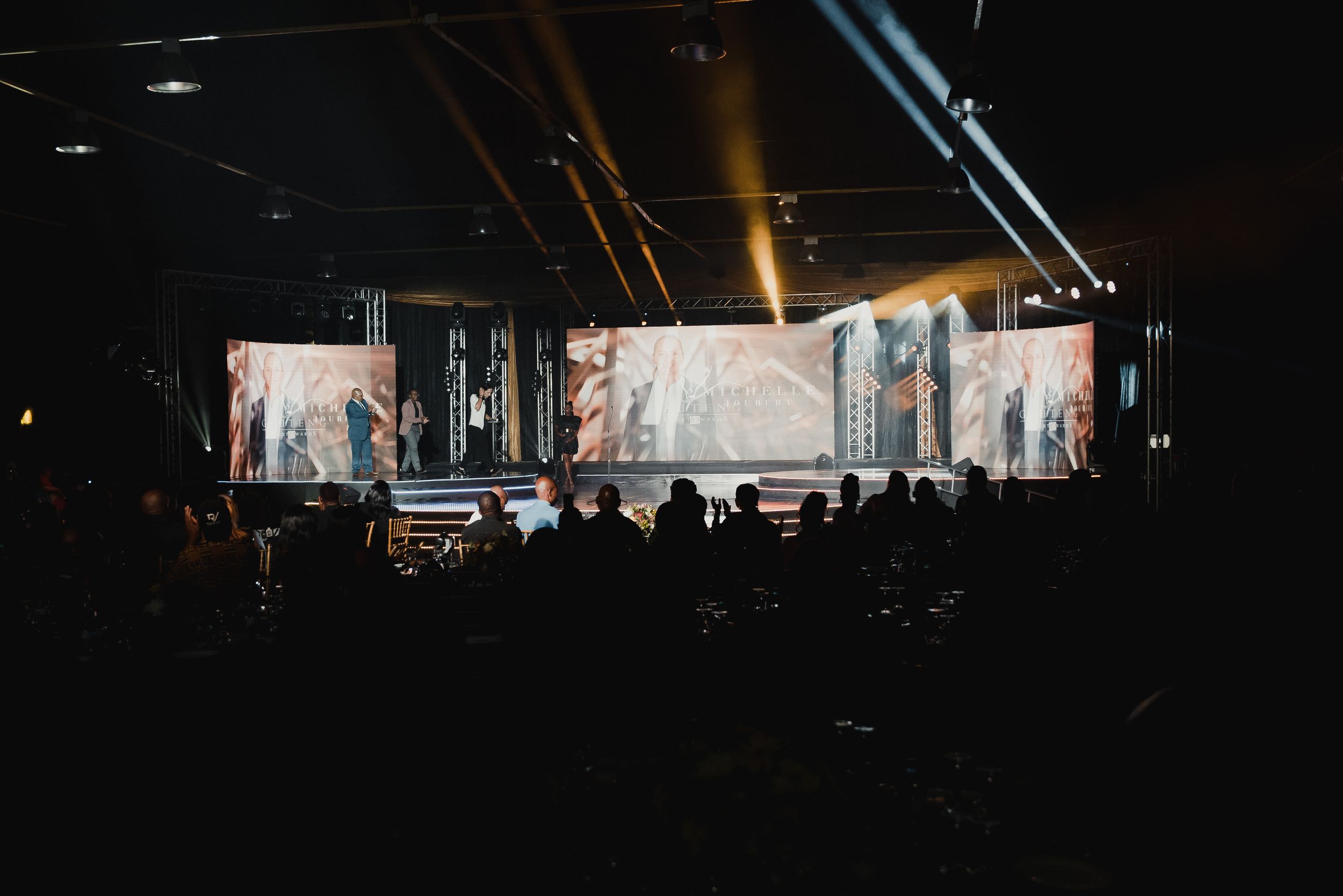 Wide concert stage setup with dramatic lighting and video displays creating an atmospheric ambiance.