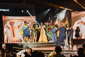 Colorful stage performance with large cast in various costumes during live show finale.
