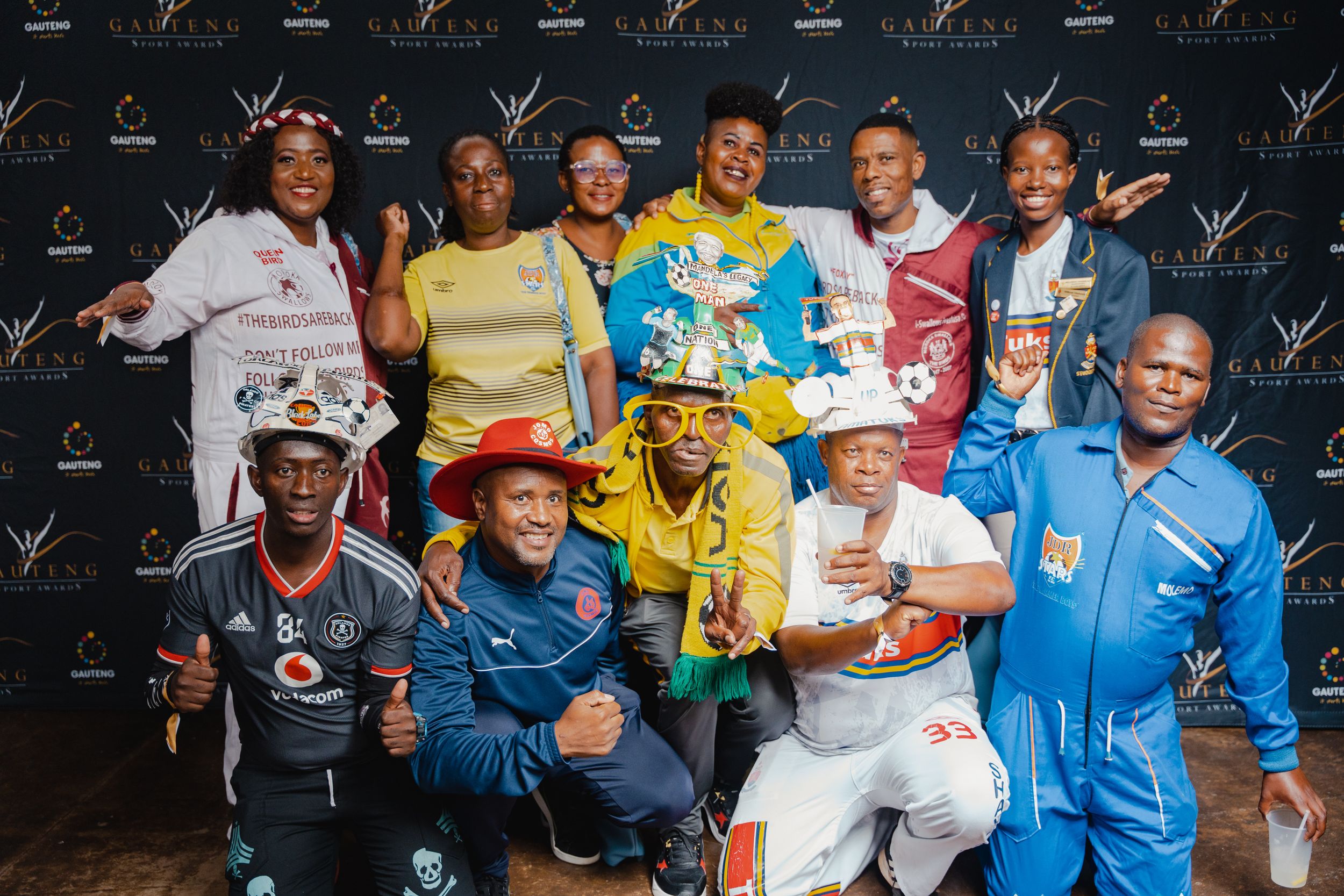 Sports team members posing together in colorful uniforms for a group photo against a branded backdrop.