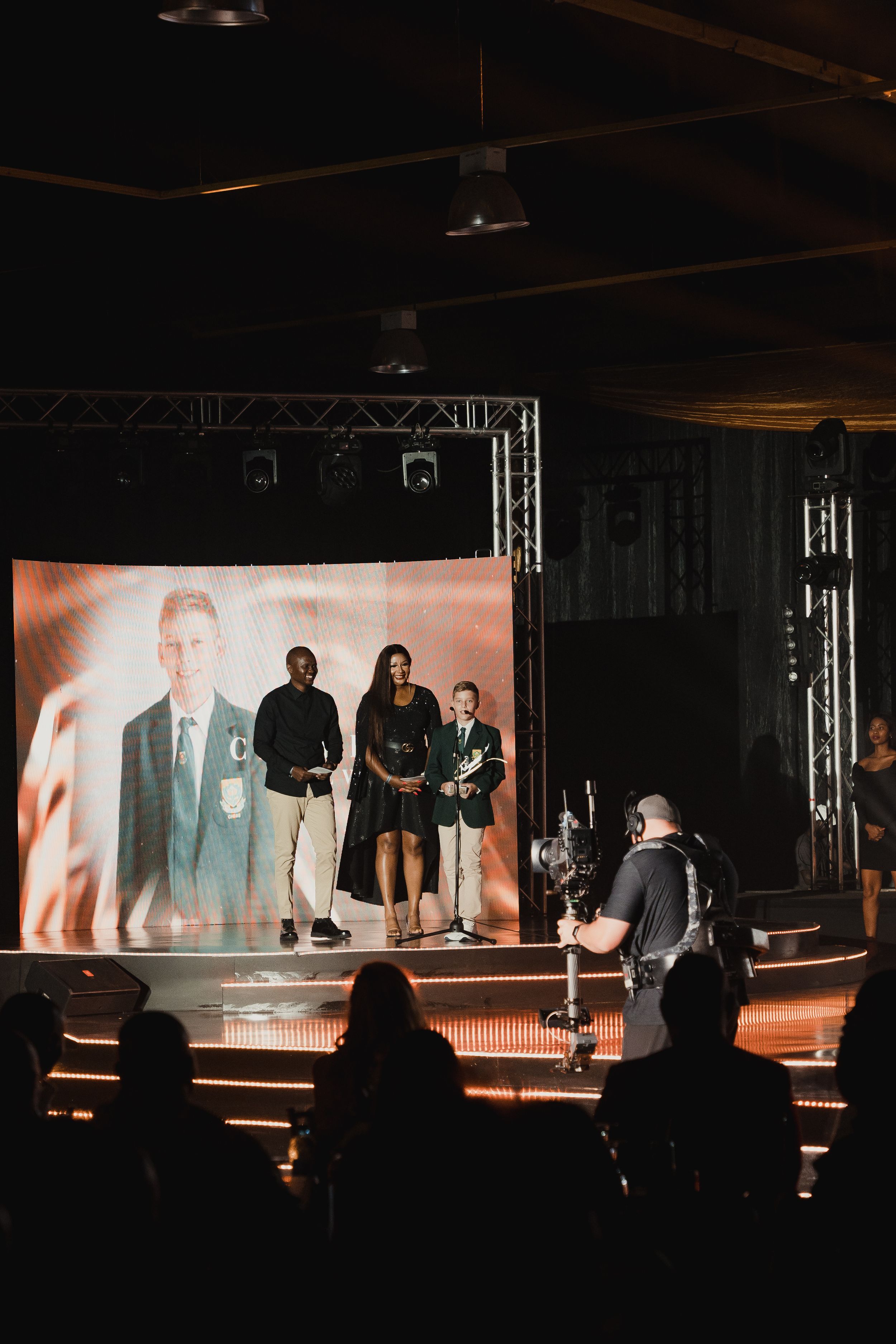 Stage performance with projected visuals and dramatic lighting showing performers on an elevated platform.