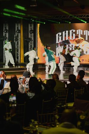 Dancers perform a choreographed routine on stage with dramatic lighting and silhouettes in front of an audience.