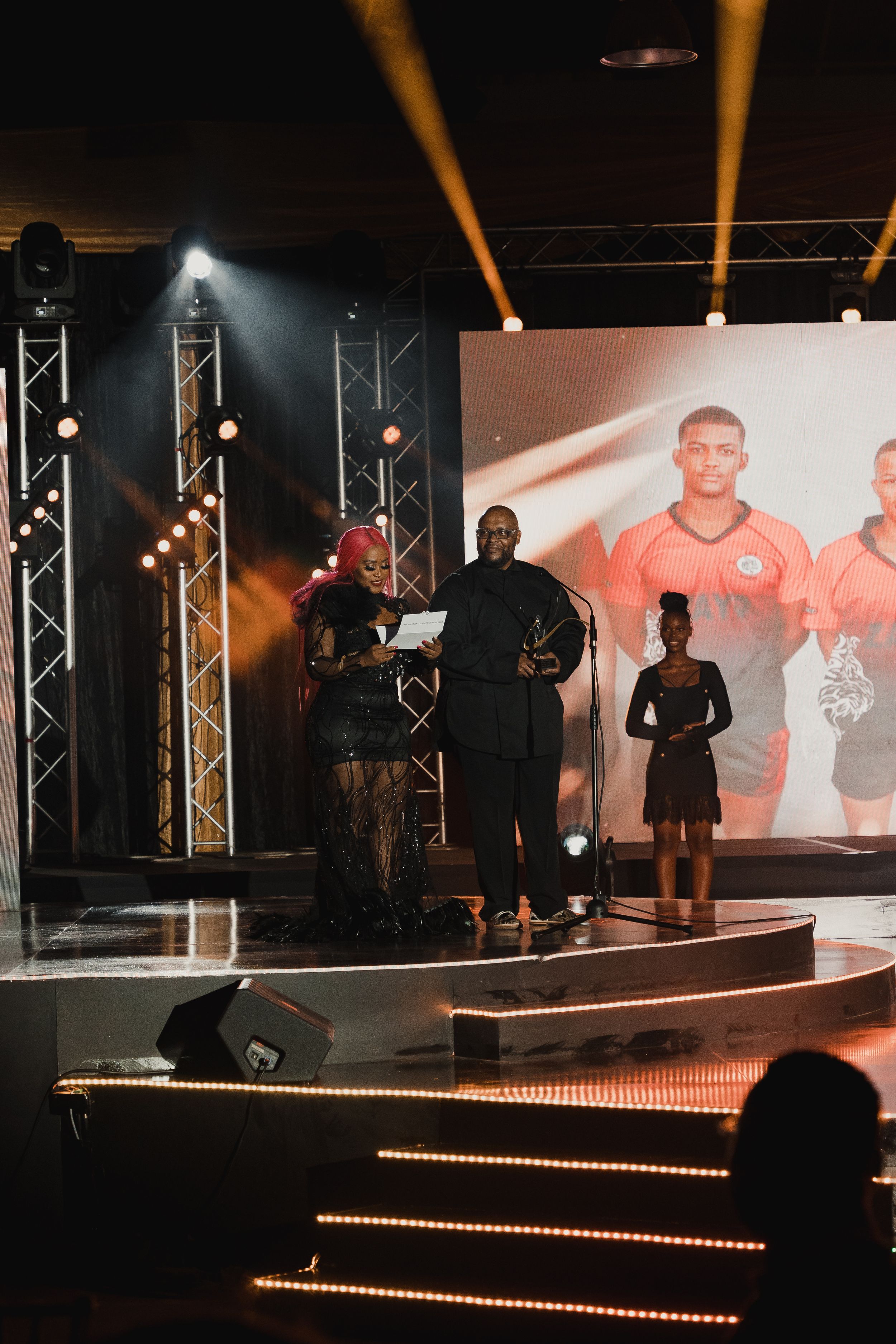 Stage performers with projected sports imagery behind them during a live event.