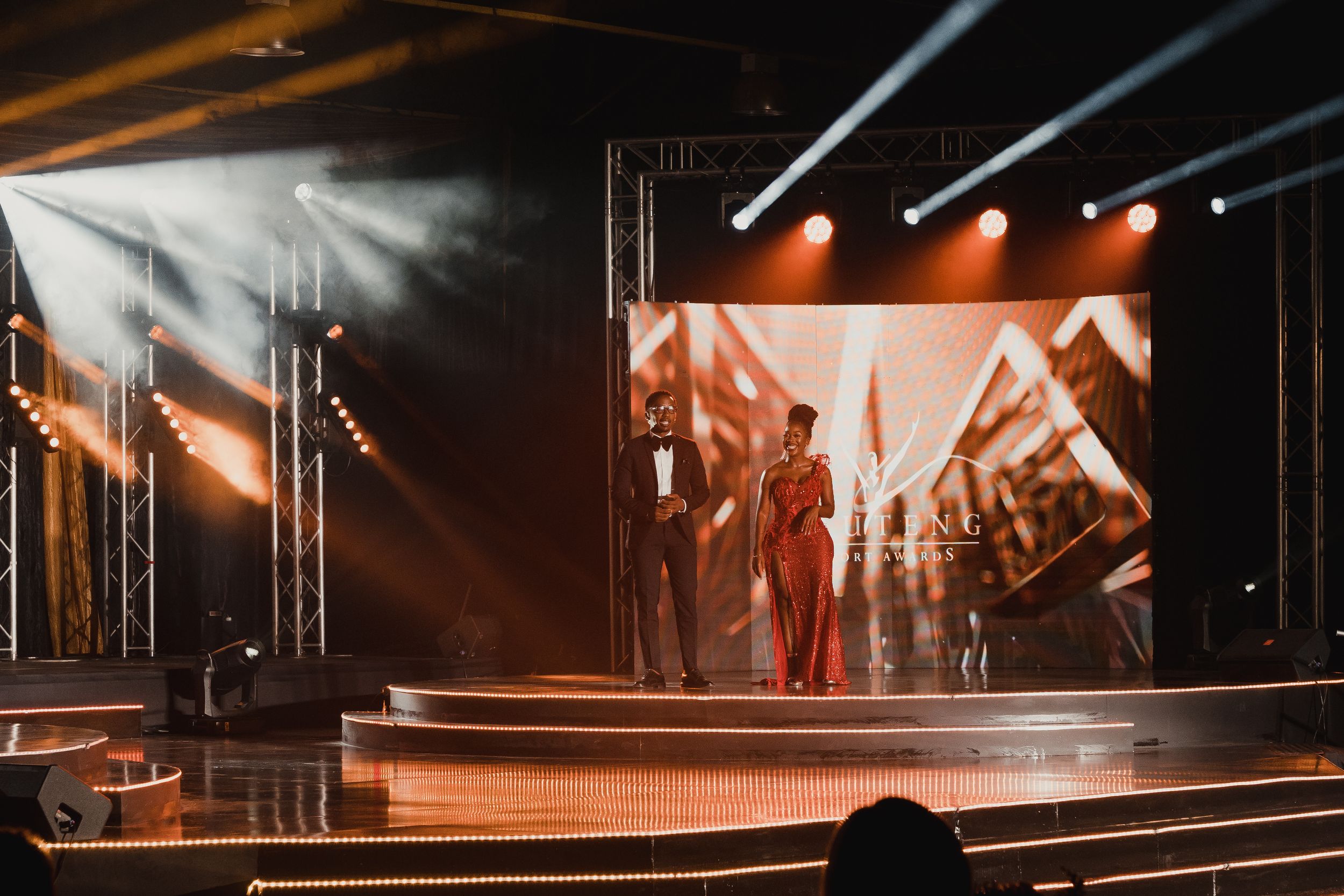 Stage performance with dramatic orange lighting and silhouetted performers on an illuminated platform.