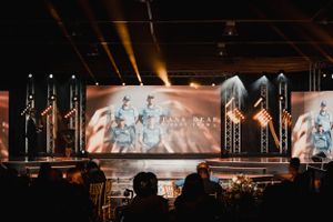 Wide concert stage setup with professional lighting rigs and large video screens displaying artistic visuals.