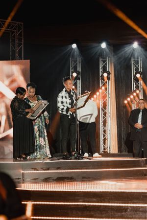 Group performance on illuminated stage with musicians and performers in formal attire.