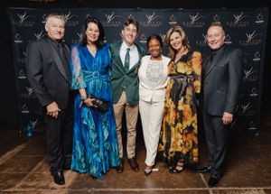 Group photo of event attendees posing against branded step-and-repeat backdrop at awards ceremony.
