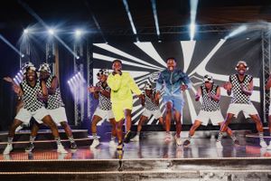 Energetic dance ensemble performing choreographed routine in colorful costumes on illuminated stage.