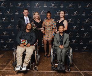 Group portrait of diverse event participants against branded backdrop at awards ceremony.