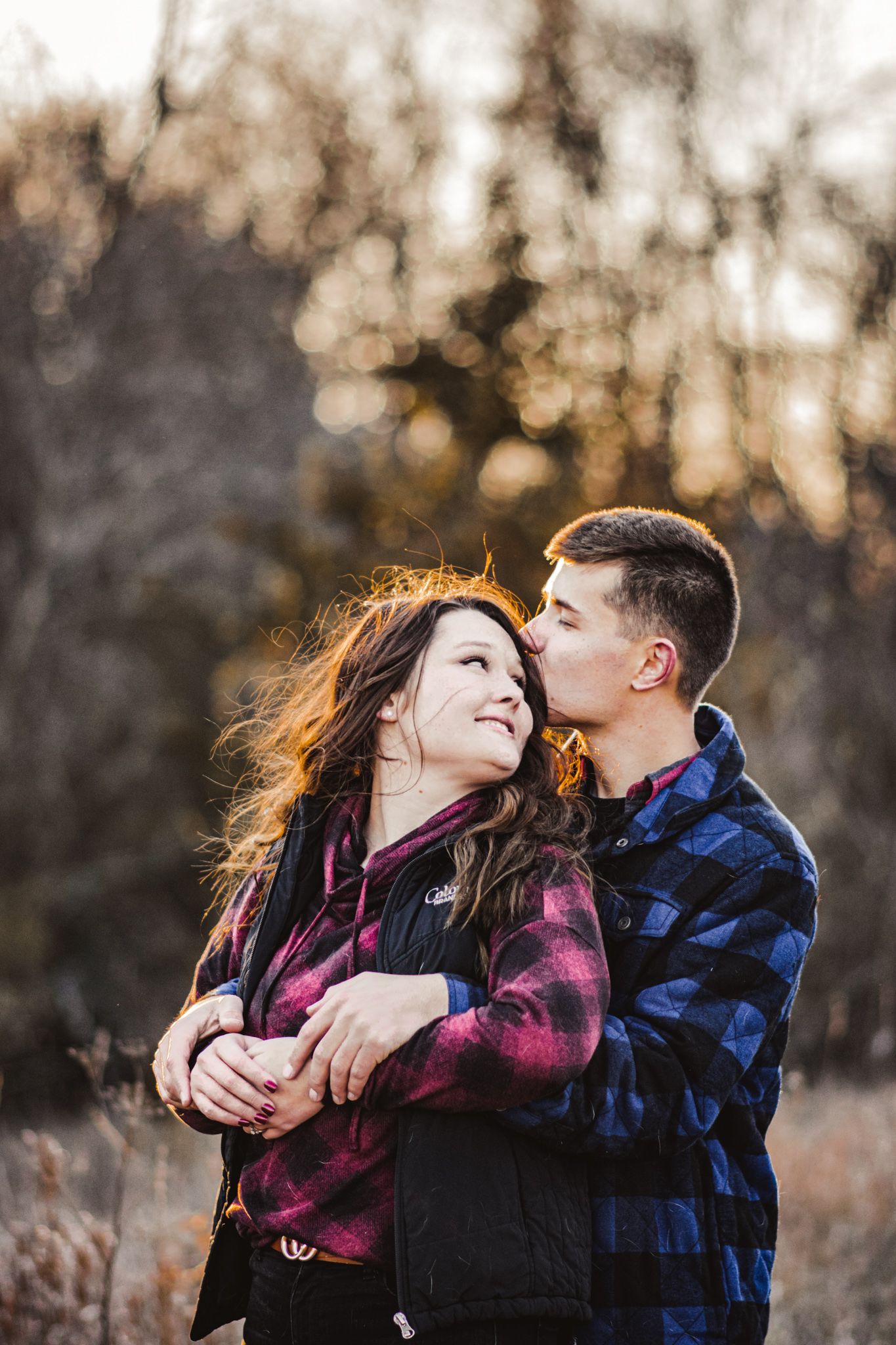A romantic outdoor portrait captured against a backdrop of sunset-lit trees.