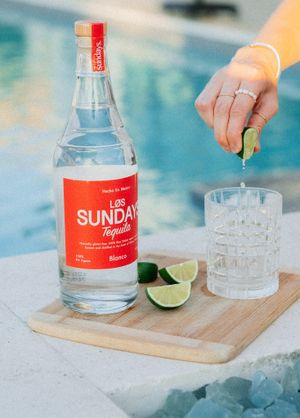 Sundays Tequila bottle and glass on wooden board with lime garnish by pool.