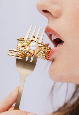 Artistic closeup of gold rings and jewelry on fork against light background.