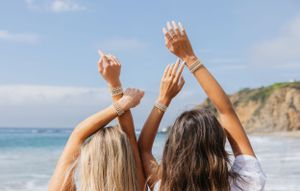 Two friends raising hands in celebration on scenic beach with cliffs.
