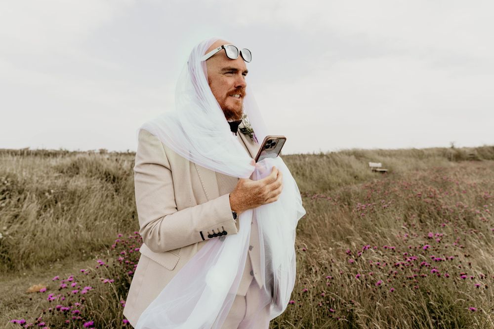 A person in a light colored outfit checking their phone while standing in a field with purple wildflowers.
