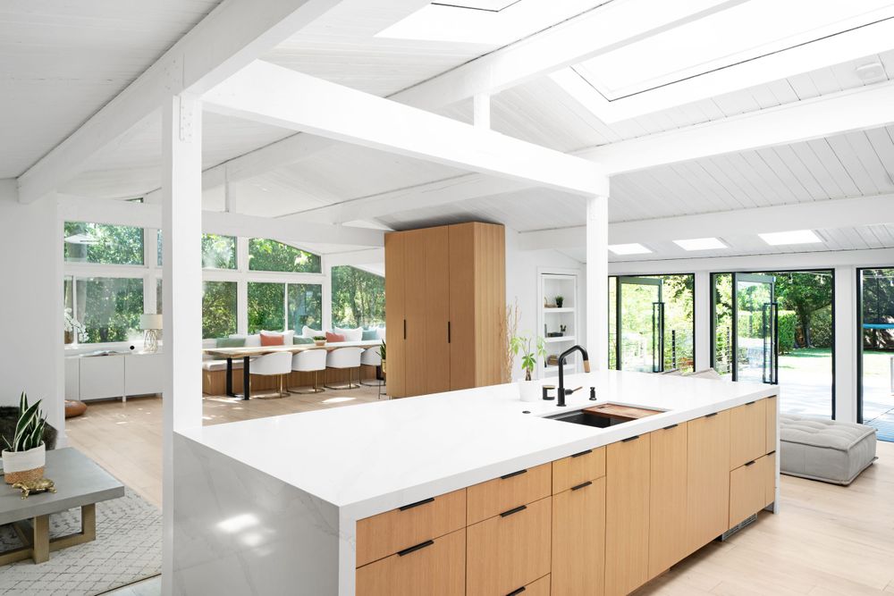 Modern white kitchen with wooden cabinets, large island and abundant natural light from skylights.