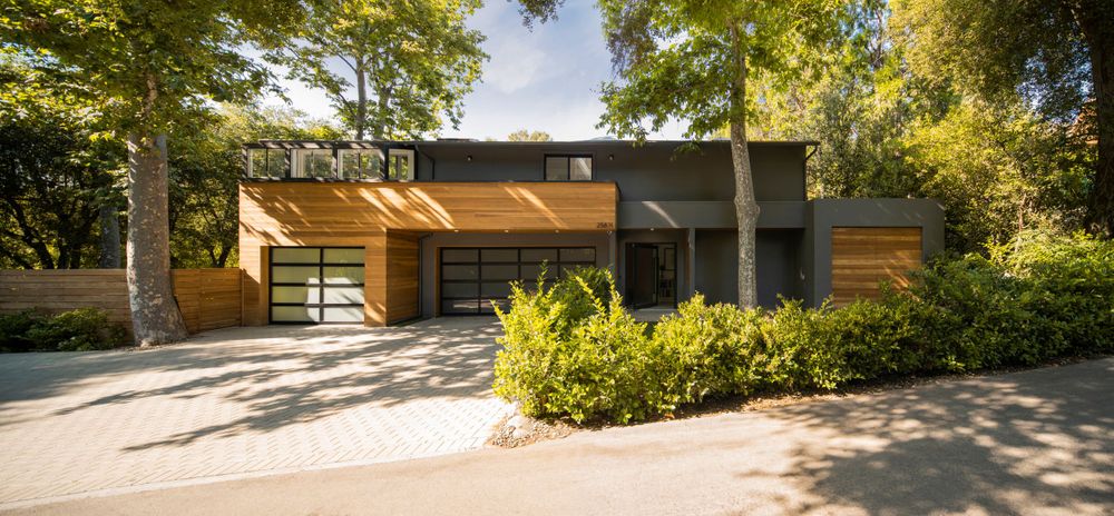 Contemporary wooden and glass facade home with landscaped entrance and carport.