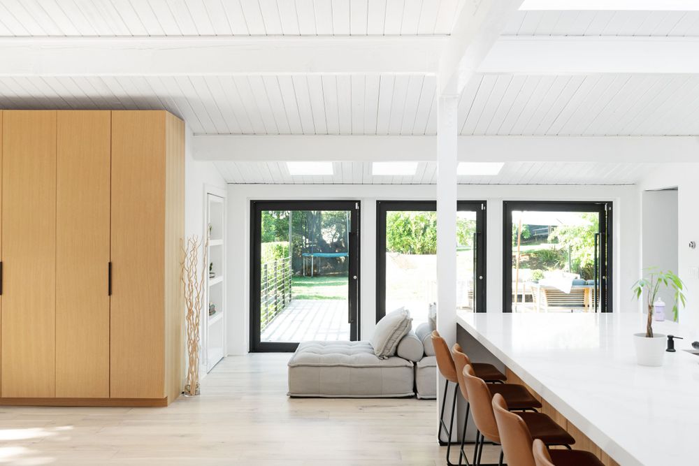 Modern open concept living space with wooden built-ins and black-framed glass doors leading to outdoor area.